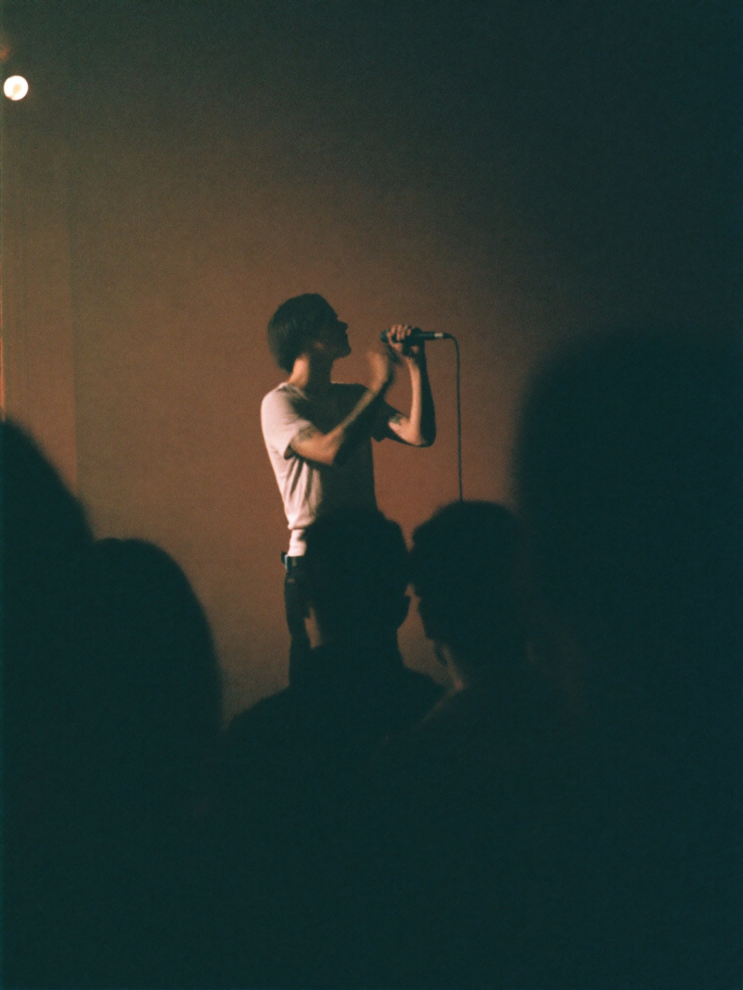 A solo artist performing on a club stage in warm amber light
